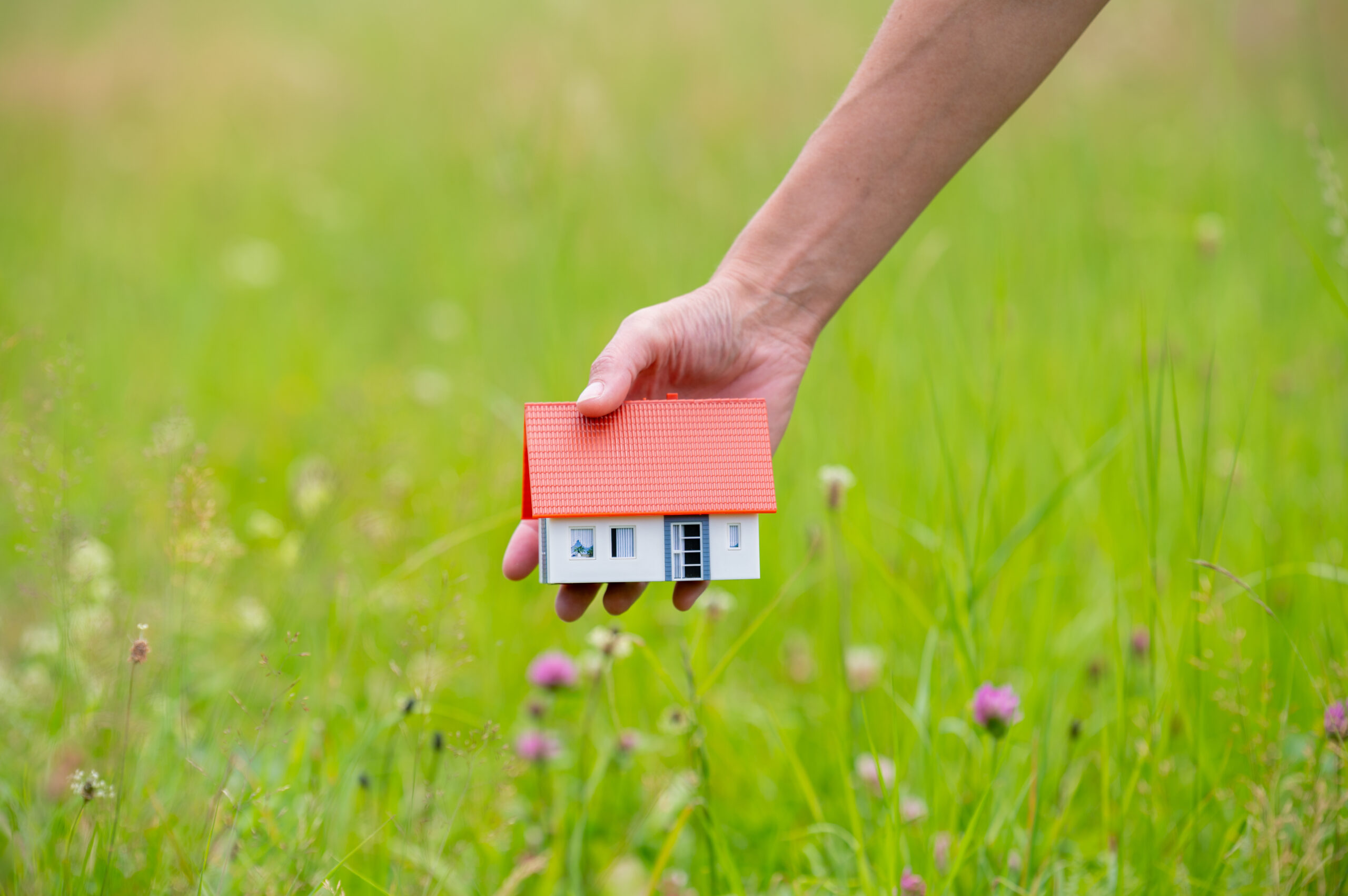 Schönes Haus als Modell auf einem Grundstück von einer Hand gehalten
