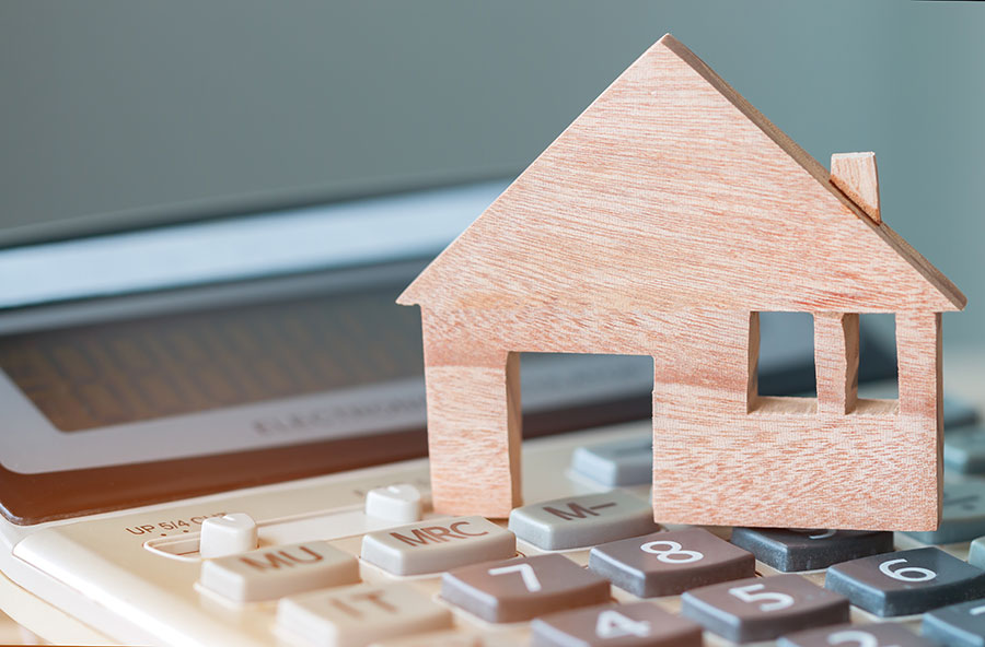 Ein Modellhaus aus Holz steht auf einem Taschenrechner.