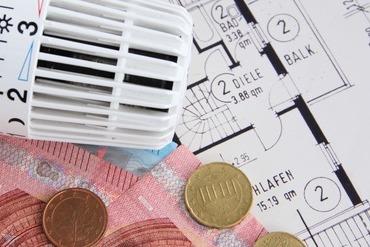 Hauspläne, darauf ein Thermostat und Euromünzen und -scheine.