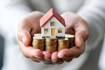 Eine Person hält Münzen und ein Modellhaus in den ausgestreckten Händen.