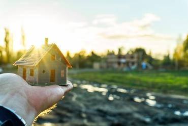 Eine Person hält ein Modellhaus in der ausgestreckten Hand.