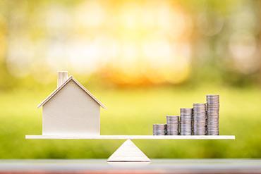 Ein Modellhaus und Münzstapel halten sich die Waage.