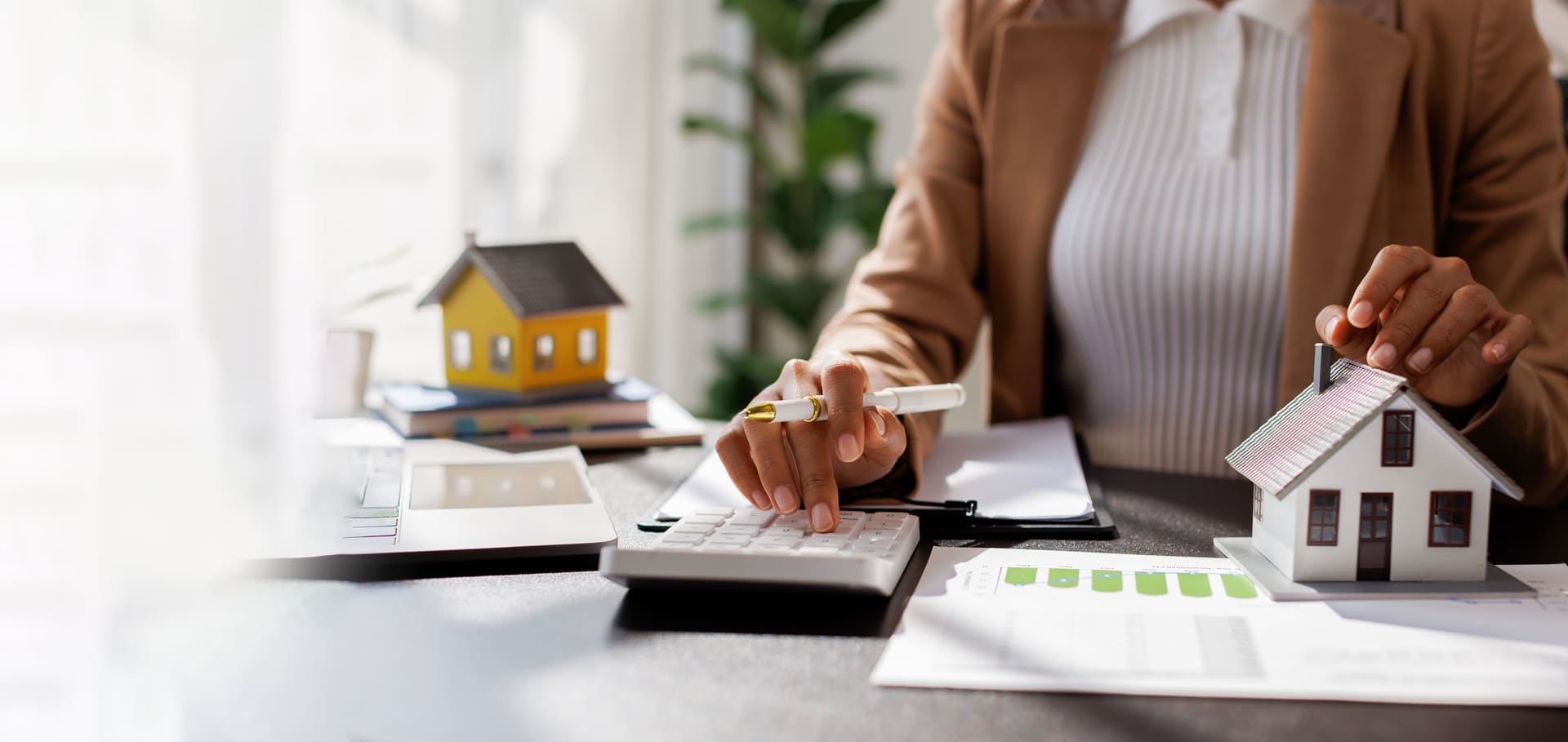 Maklerin arbeitet mit Taschenrechner und Modellhaus an Finanzierung und Immobilienunterlagen.
