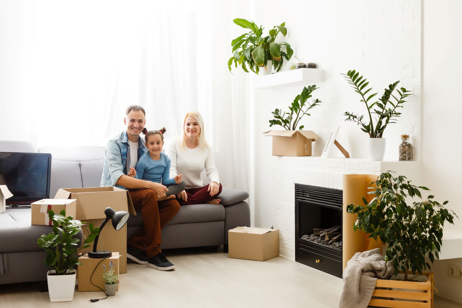 Familie mit Mädchen auf Sofa, umgeben von Umzugskartons und Pflanzen.