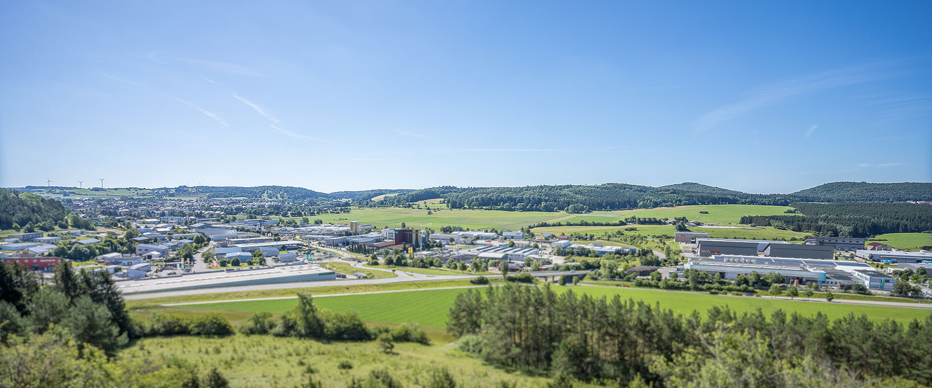 Panoramablick auf eine Stadt mit Industriegebieten, Feldern und bewaldeten Hügeln unter klarem Himmel