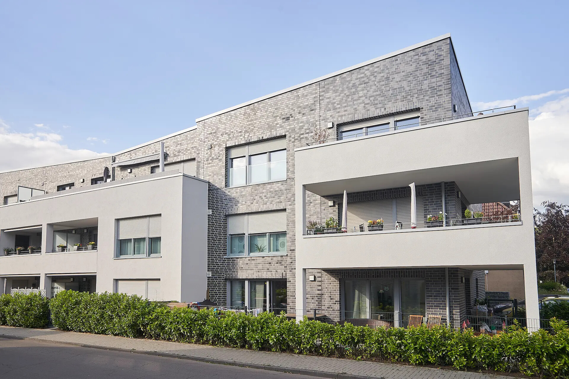Wohnung mit Balkonen, große Fenster, Backstein und weiße Fassade.