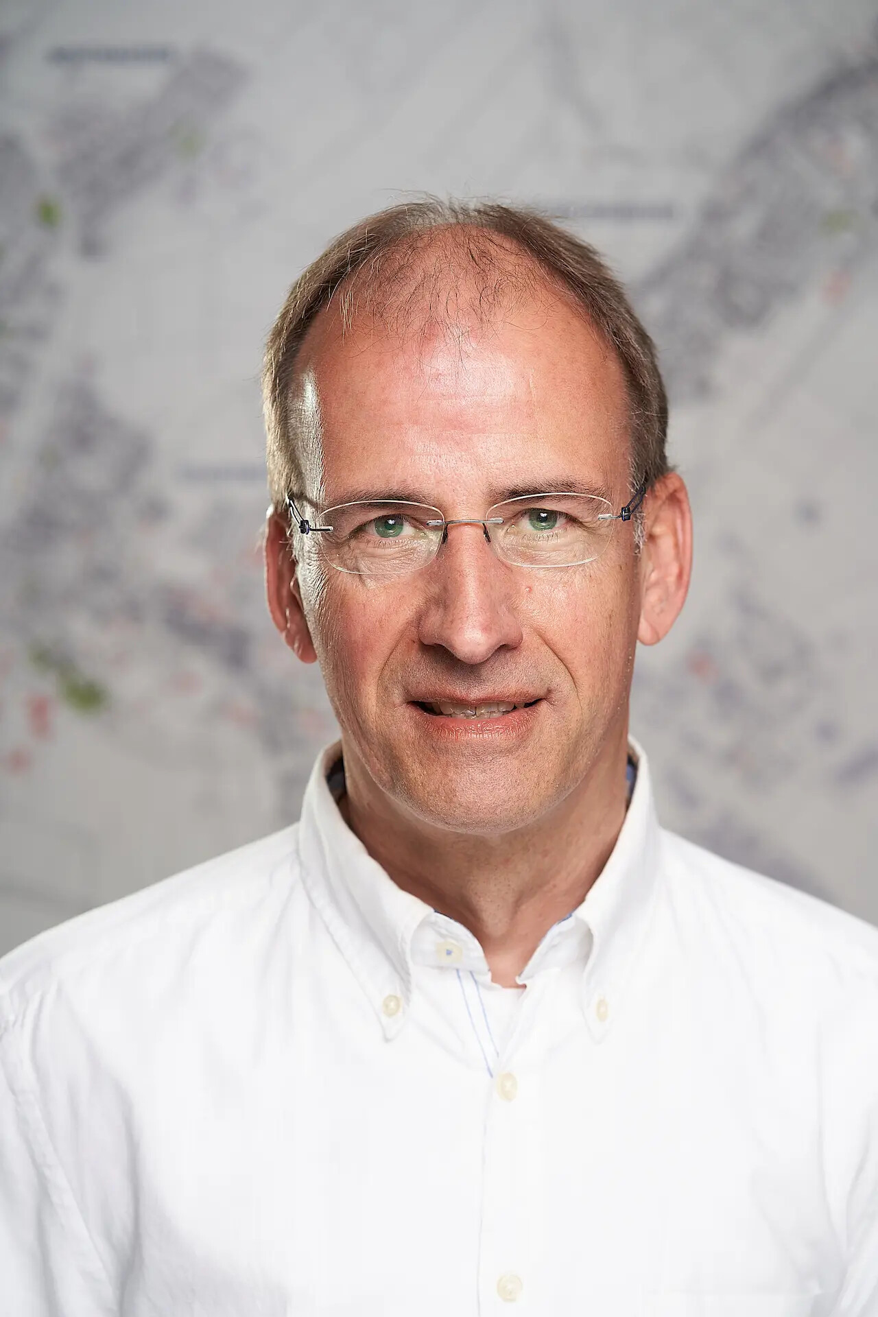 Uwe Wiegand mit Brille und weißem Hemd vor unscharfer Kartenkulisse.