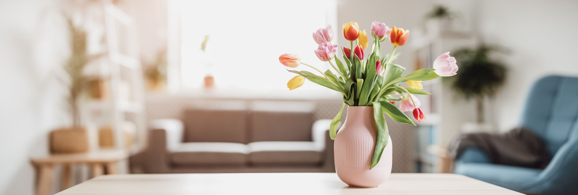 Rosa Vase mit bunten Tulpen auf einem Tisch im Wohnzimmer.