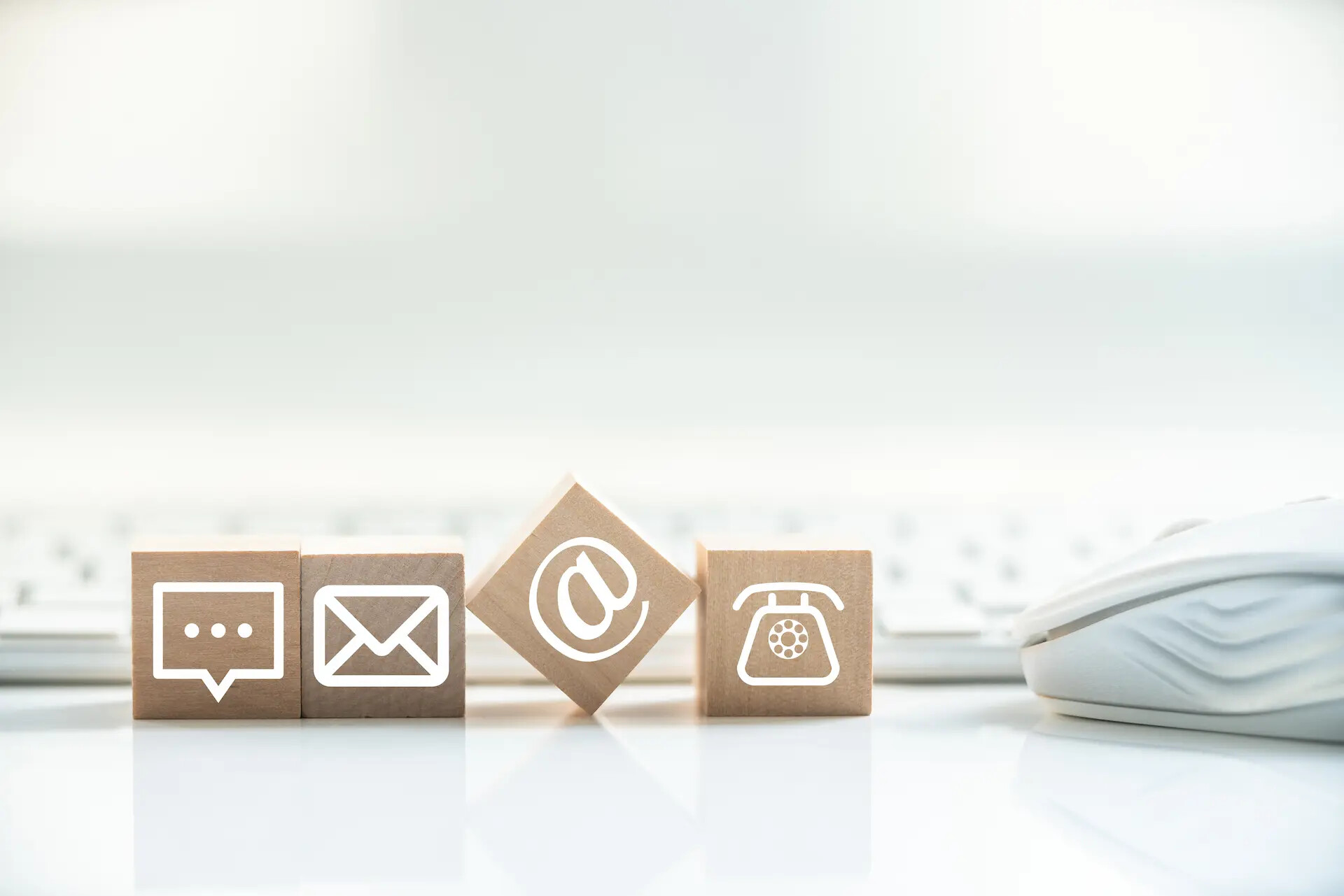 Holzblöcke mit Chat-, E-Mail-, @- und Telefon-Icons vor Tastatur.