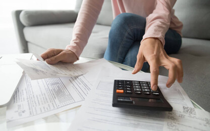 Frau mit Taschenrechner und Rechnungen auf dem Tisch: Beitragsbild Corona & Wohnungsmiete