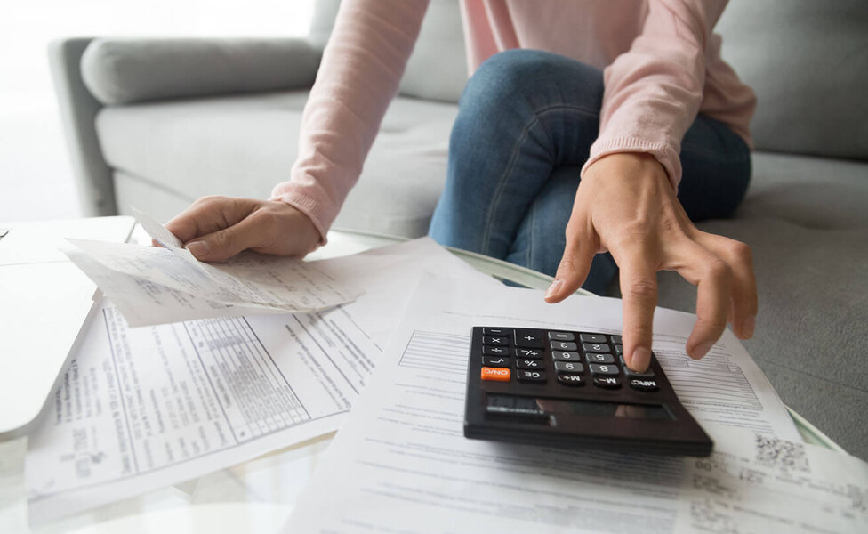 Frau mit Taschenrechner und Rechnungen auf dem Tisch: Beitragsbild Corona & Wohnungsmiete