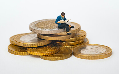 Miniaturfigur sitzt auf Münzen und liest