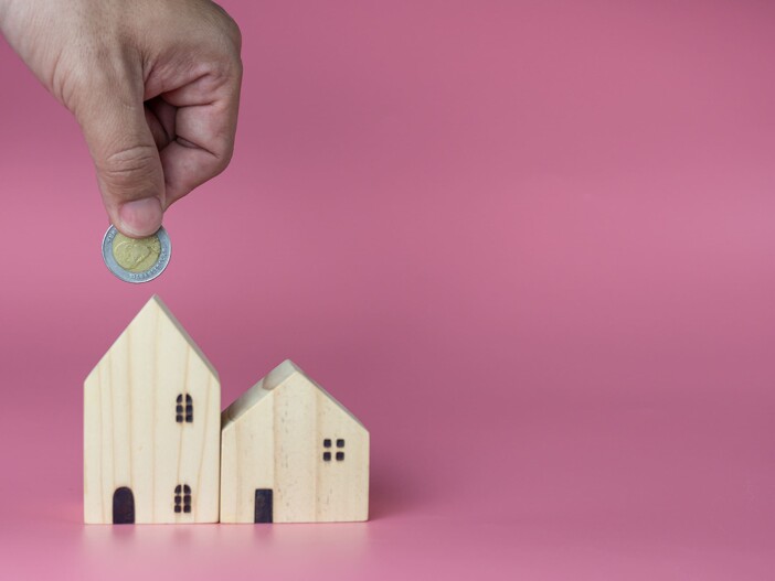 Ein Person mit einer Münze in der Hand und Hausmodell aus Holz