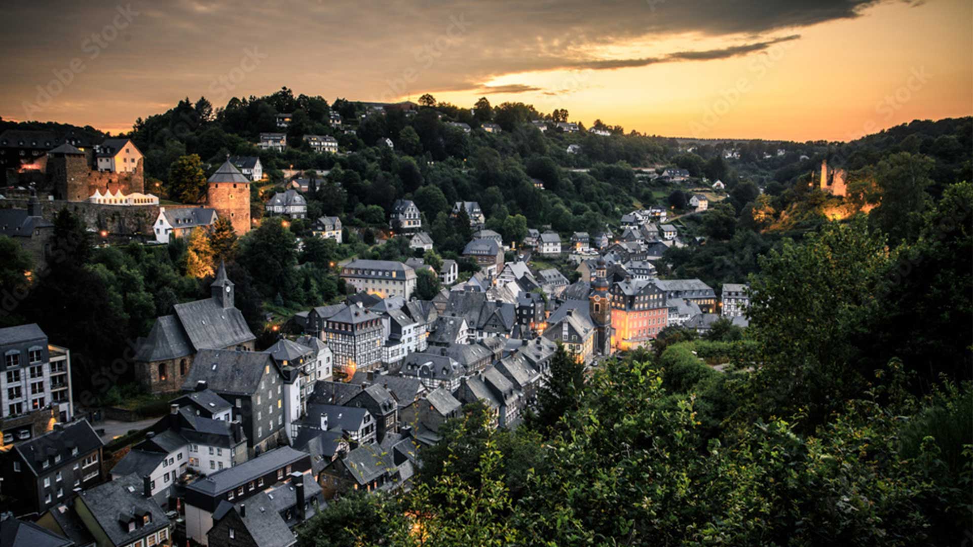 Stadt am Hang bei Sonnenuntergang, Häuser und Bäume unter einem glühenden Himmel.