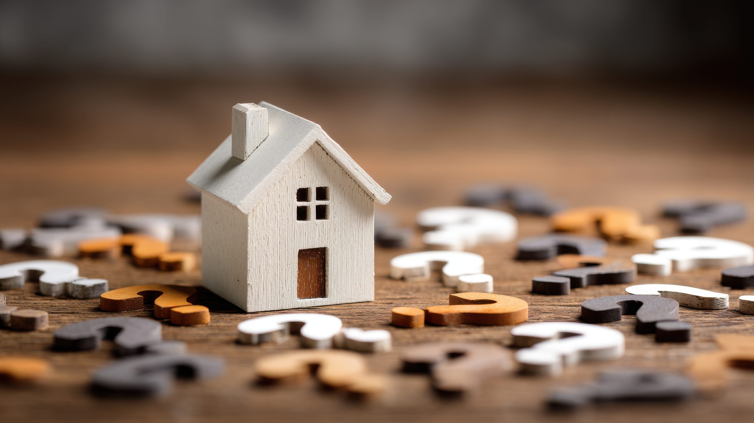 Kleines Holzhaus und verstreute Fragezeichen aus Holz auf Tisch.