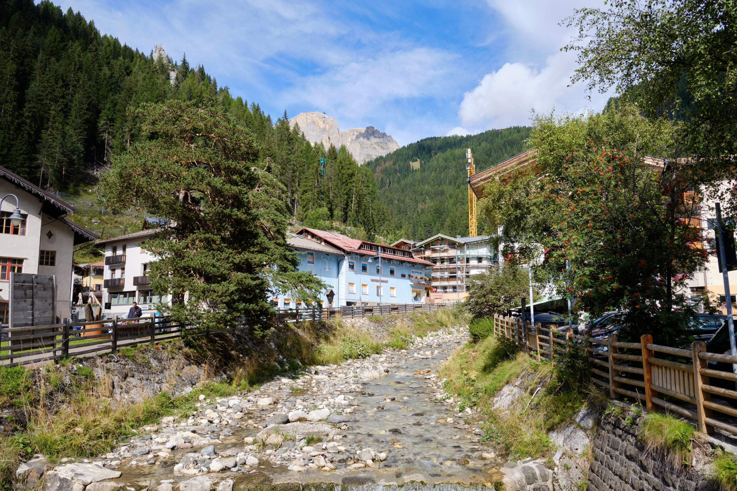Rocky stream passes colorful village, trees, and distant mountains.