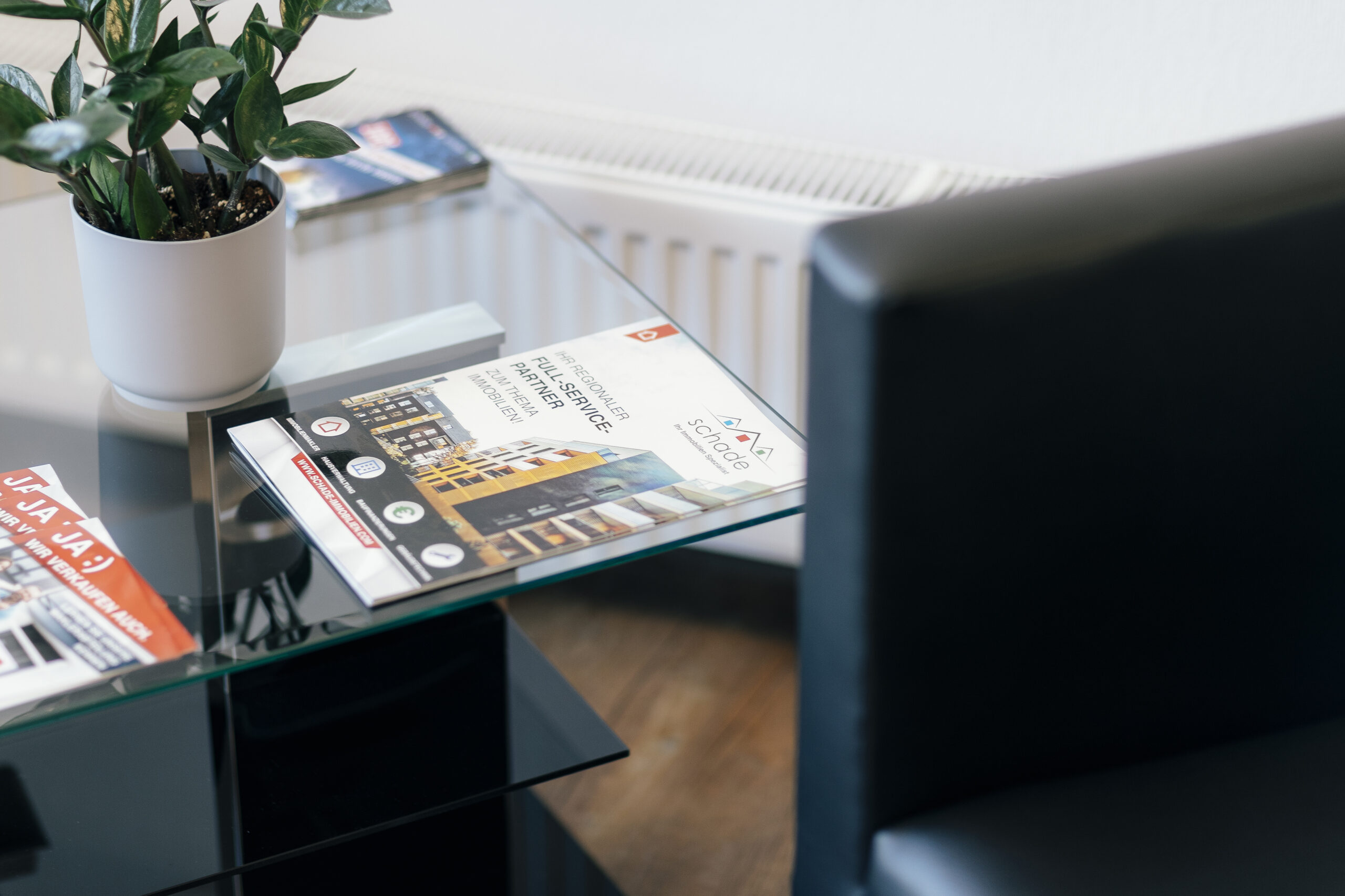 Glastisch mit Zeitschriften, Pflanze und schwarzem Stuhl im Büro.
