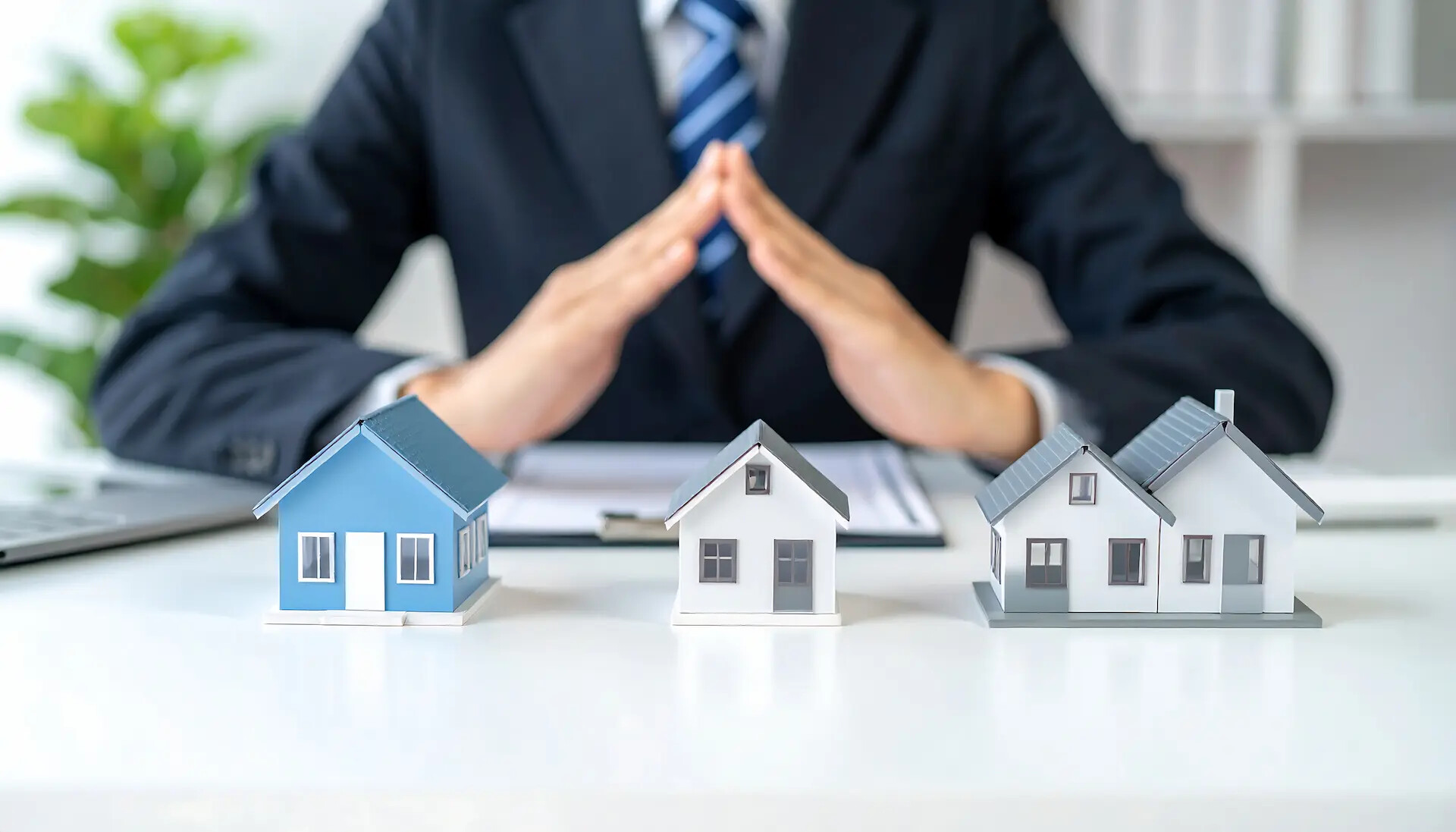 Person im Anzug hinter Modellhäusern auf Schreibtisch.