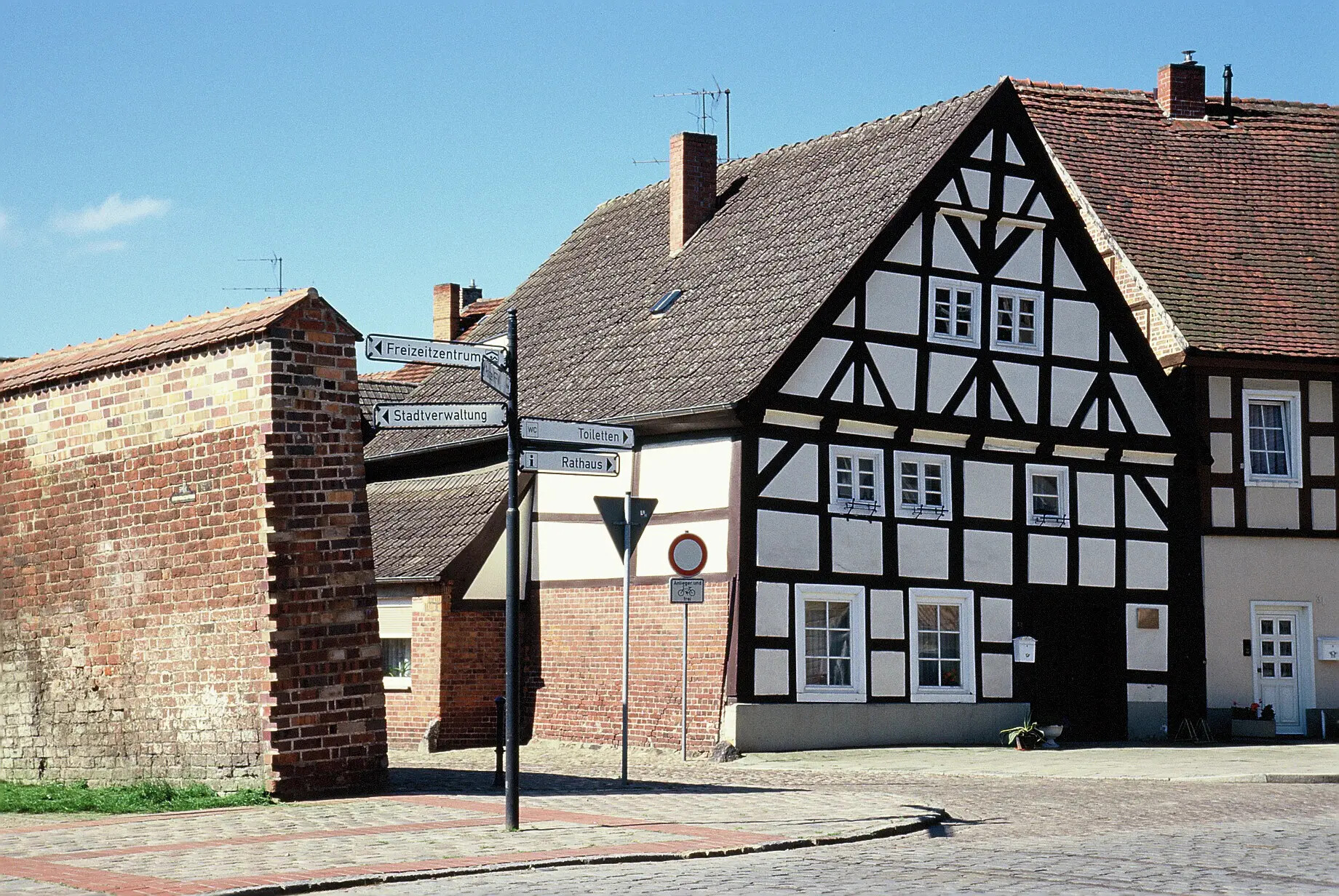 Fachwerkhaus hinter Backsteinmauer und Straßenschildern.