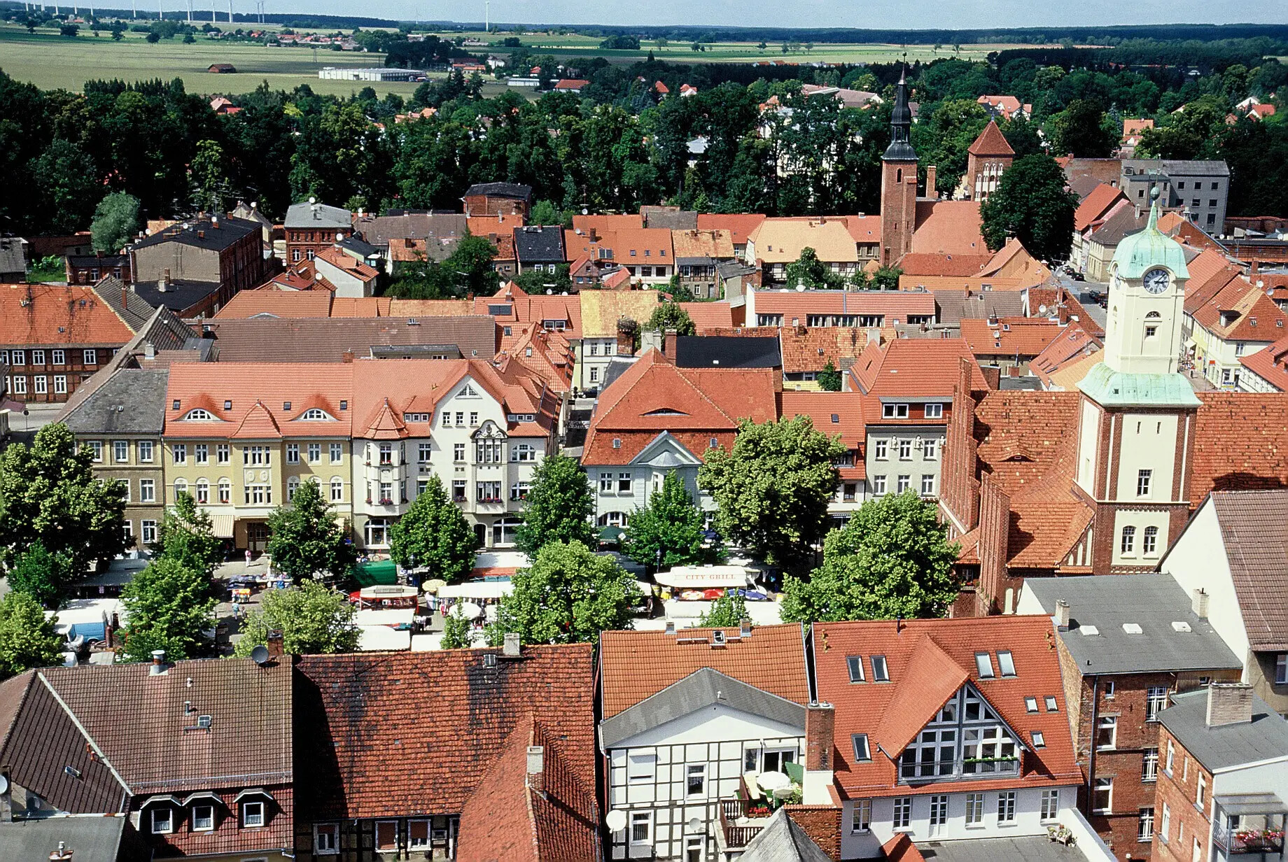 Stadt mit roten Dächern, Uhrturm und grünem Platz von oben.