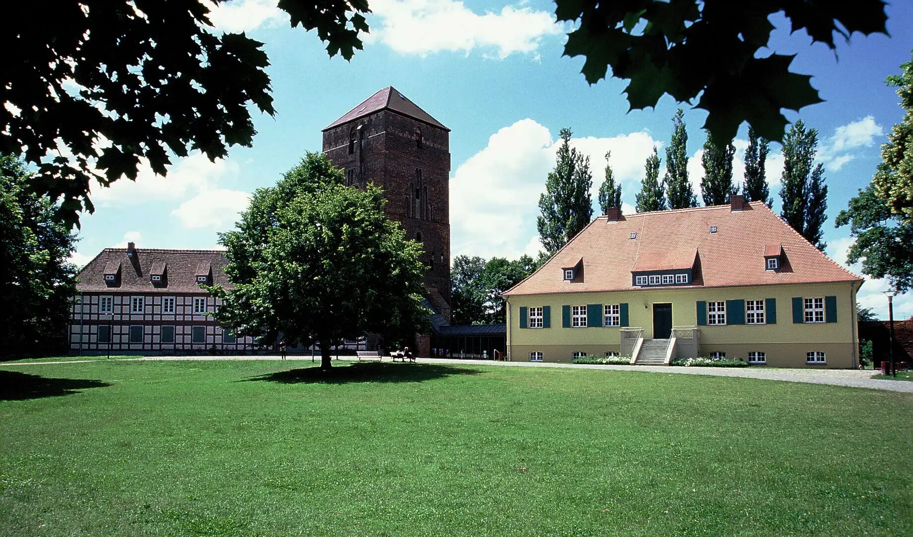 Grüner Rasen, historische Gebäude und ein hoher Turm unter blauem Himmel.