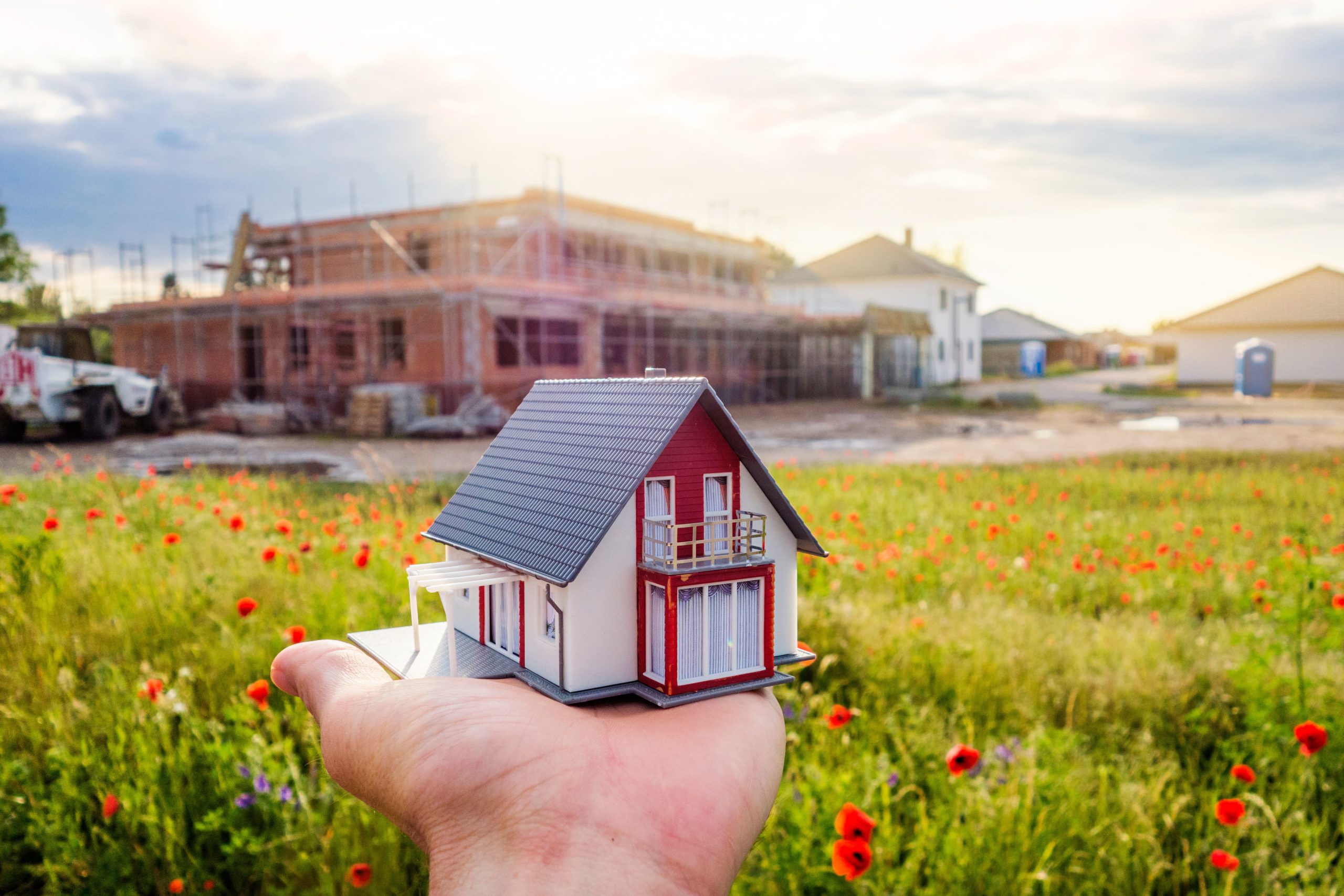 Mann hält ein kleines Modellhaus vor seinen Neubau