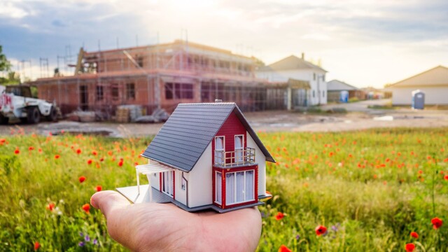 Mann hält ein kleines Modellhaus vor seinen Neubau