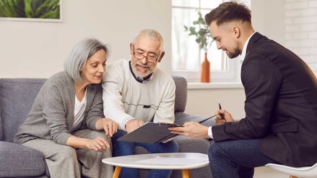 Älteres Ehepaar wird im Wohnzimmer vom Makler zum Ablauf beim Immobilienkauf beraten