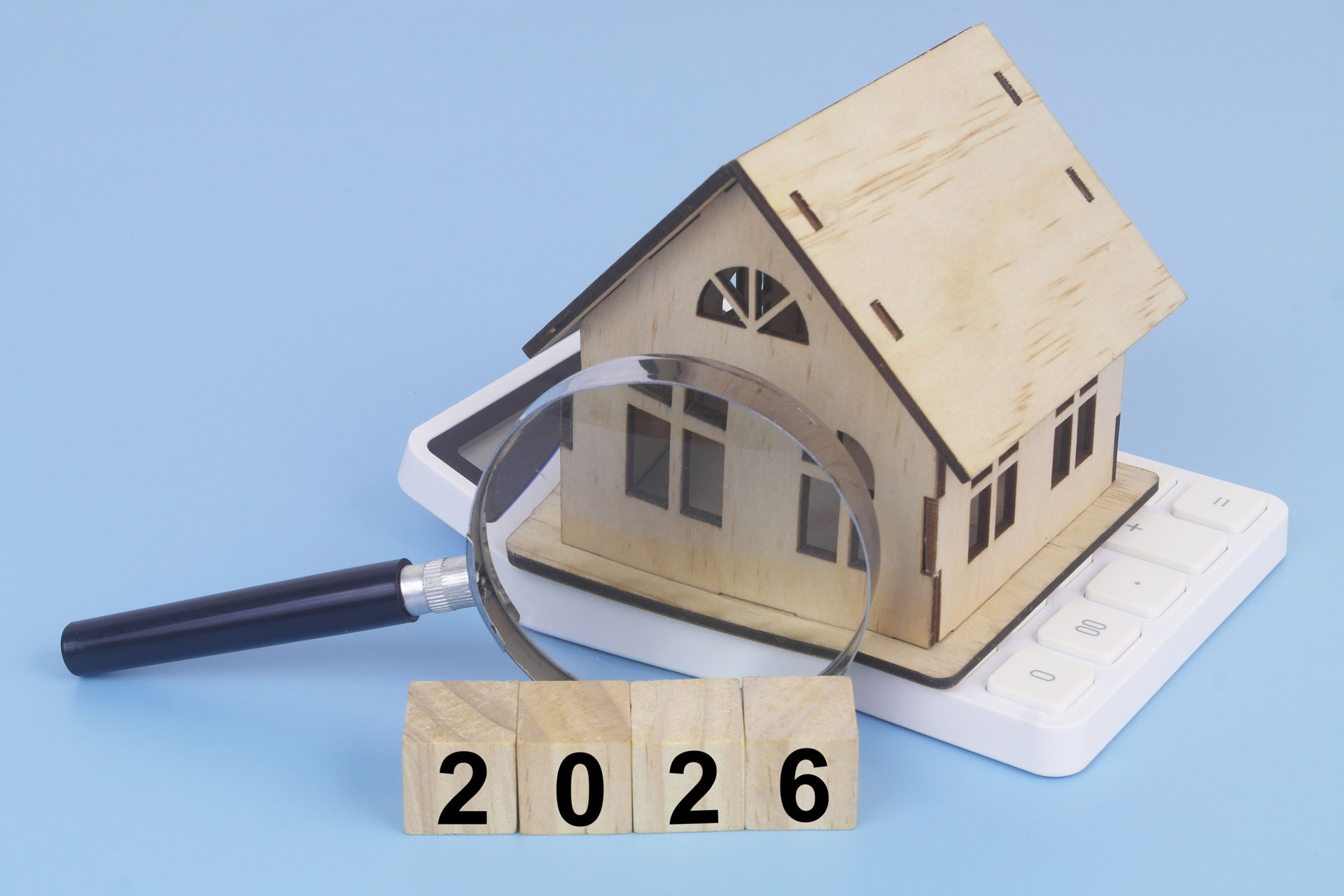 Modellhaus, Taschenrechner, Lupe und Holzwürfel mit der Zahl 2026: Symbolisiert Immobilienpreise