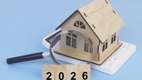 Modellhaus, Taschenrechner, Lupe und Holzwürfel mit der Zahl 2026: Symbolisiert Immobilienpreise