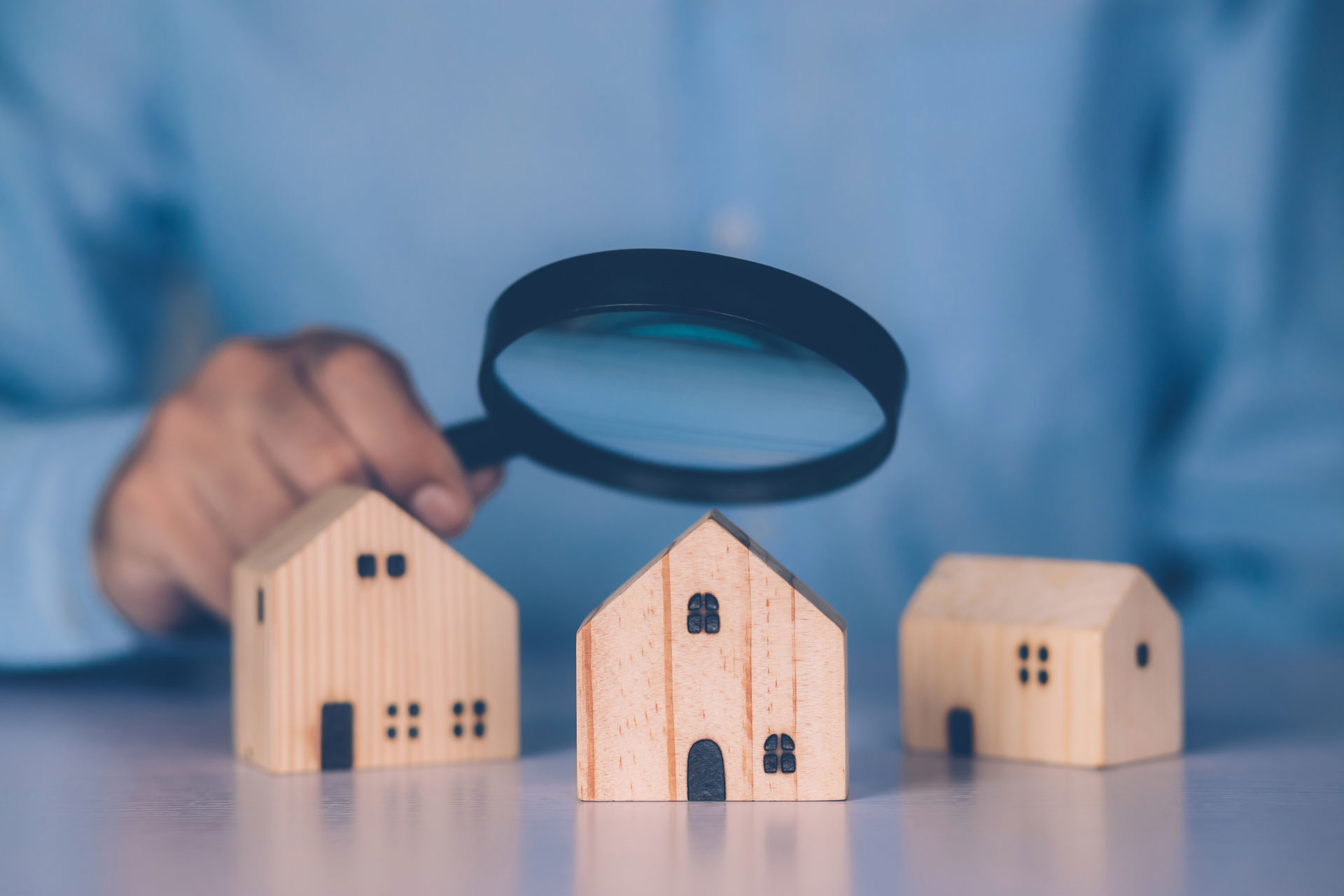 Person hält Lupe auf Modellhäuser: Vergleich Immobilienwert in Boye und Klein Hehlen