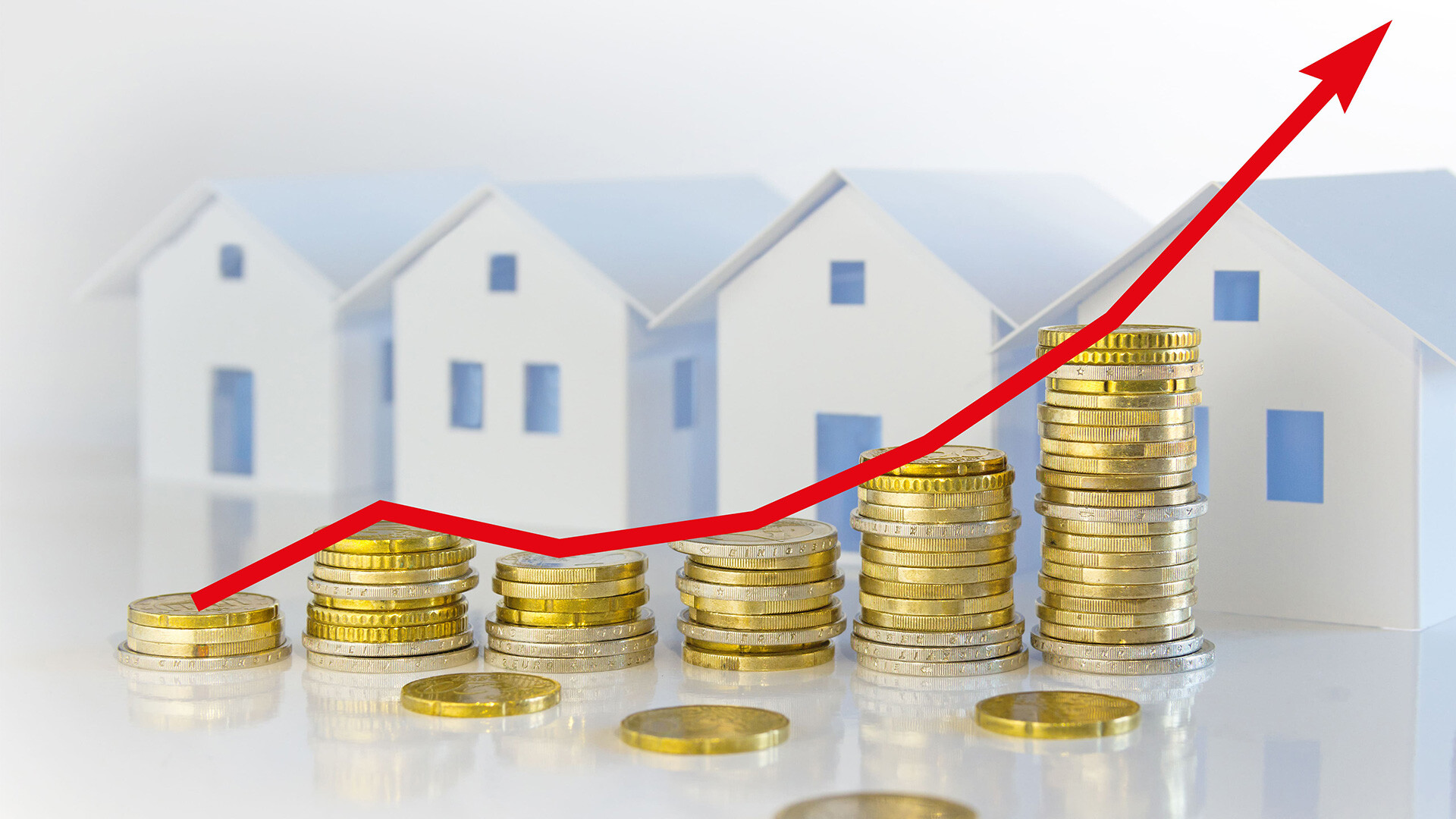 Steigende Münzstapel, roter Pfeil, Häuser im Hintergrund: Symbol für Kapitalanlagen