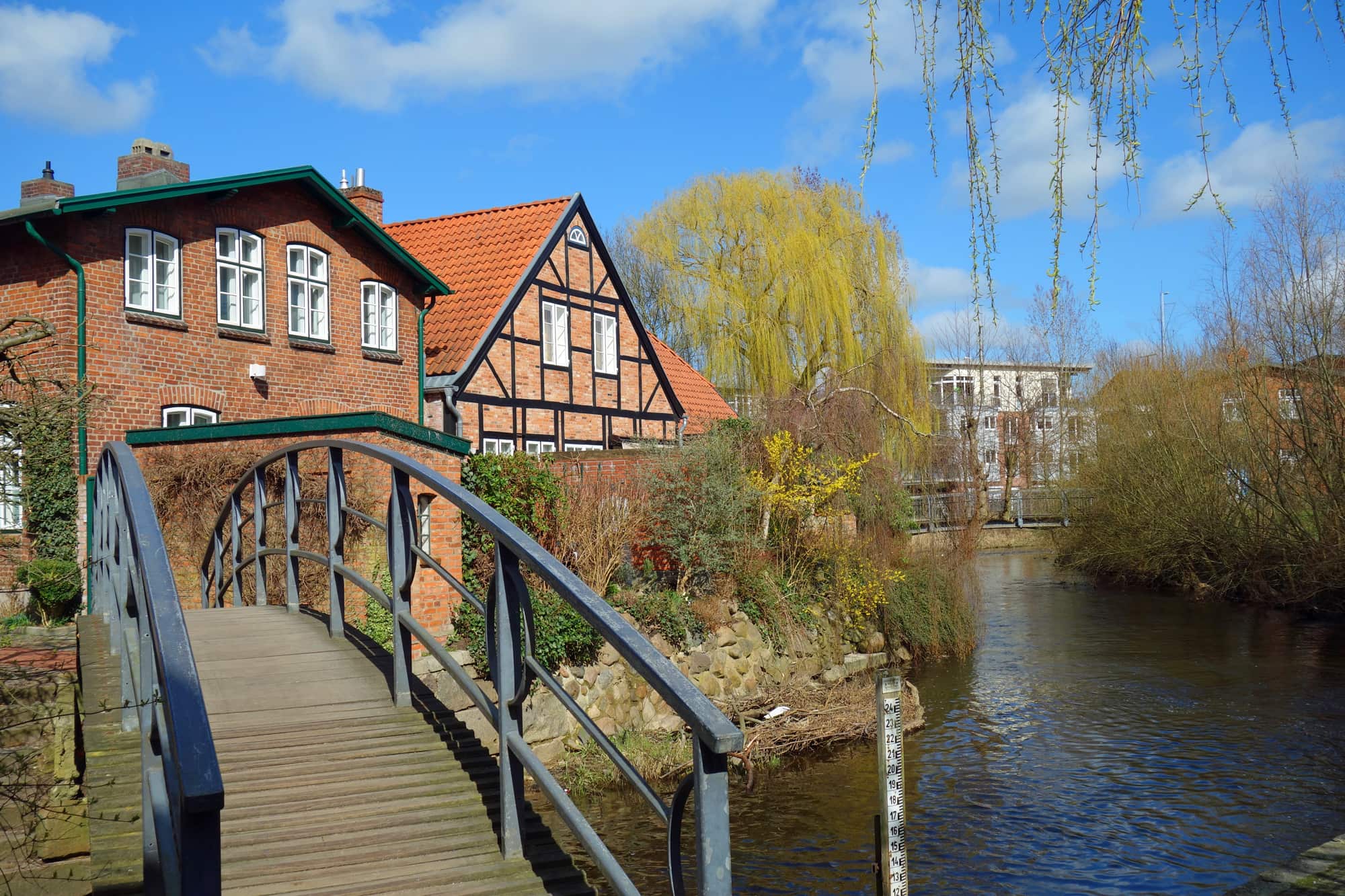 Bogenbrücke zu Ziegel- und Holzhäusern an einem ruhigen Fluss.