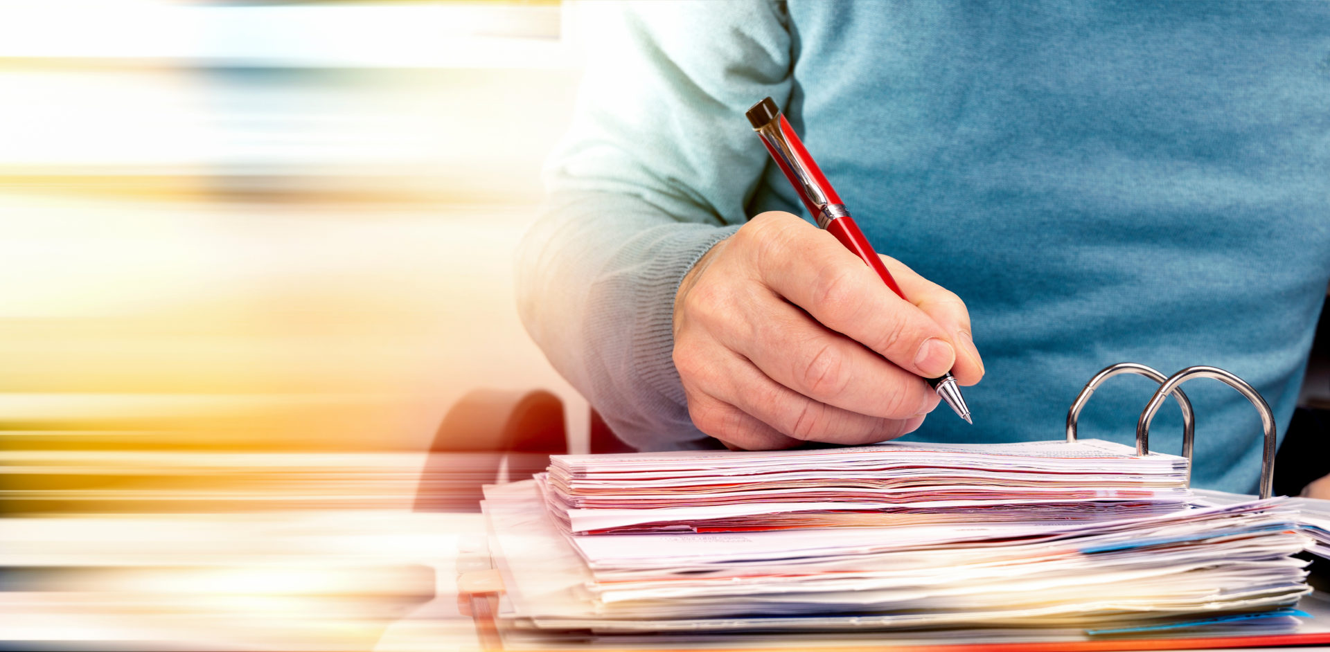 Person in blauem Pullover schreibt auf Unterlagen in einem Ordner