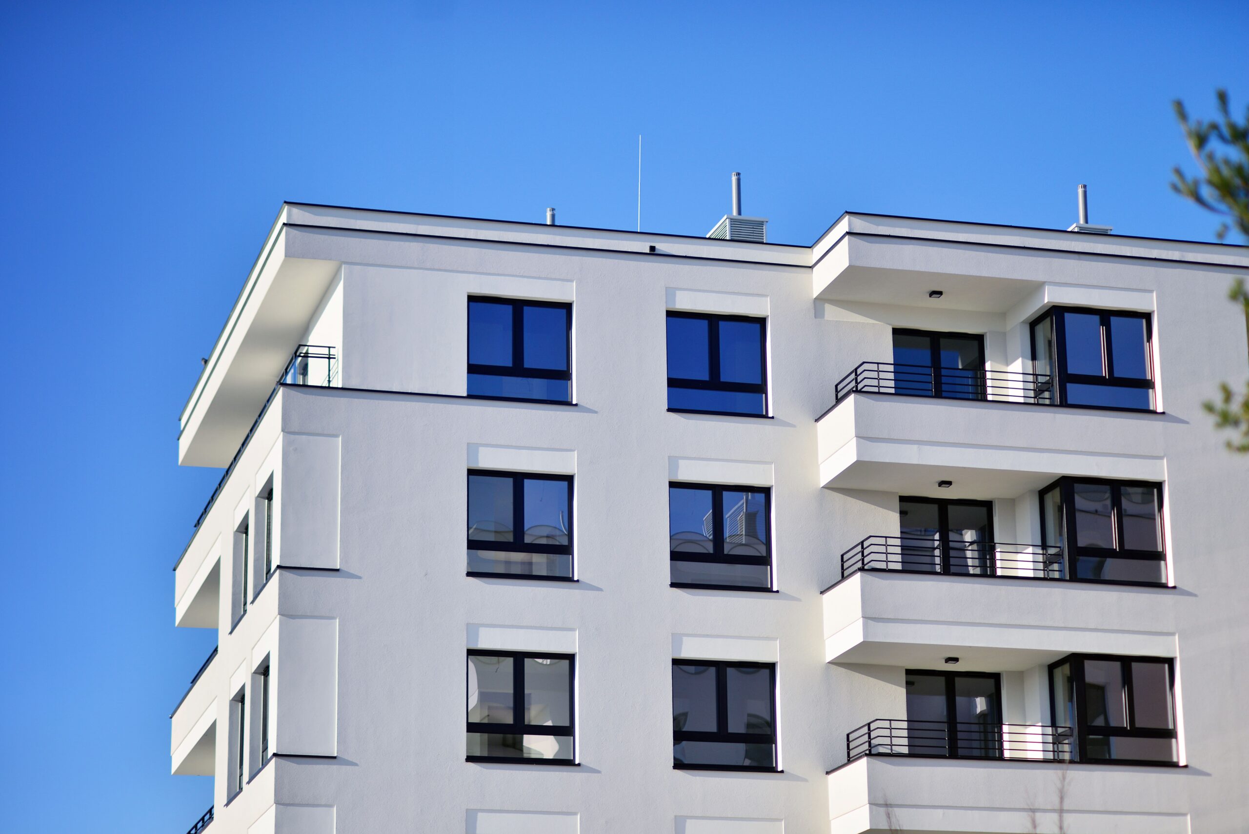 Weißes Mehrfamilienhaus mit Balkonen, großen Fenstern, blauem Himmel.