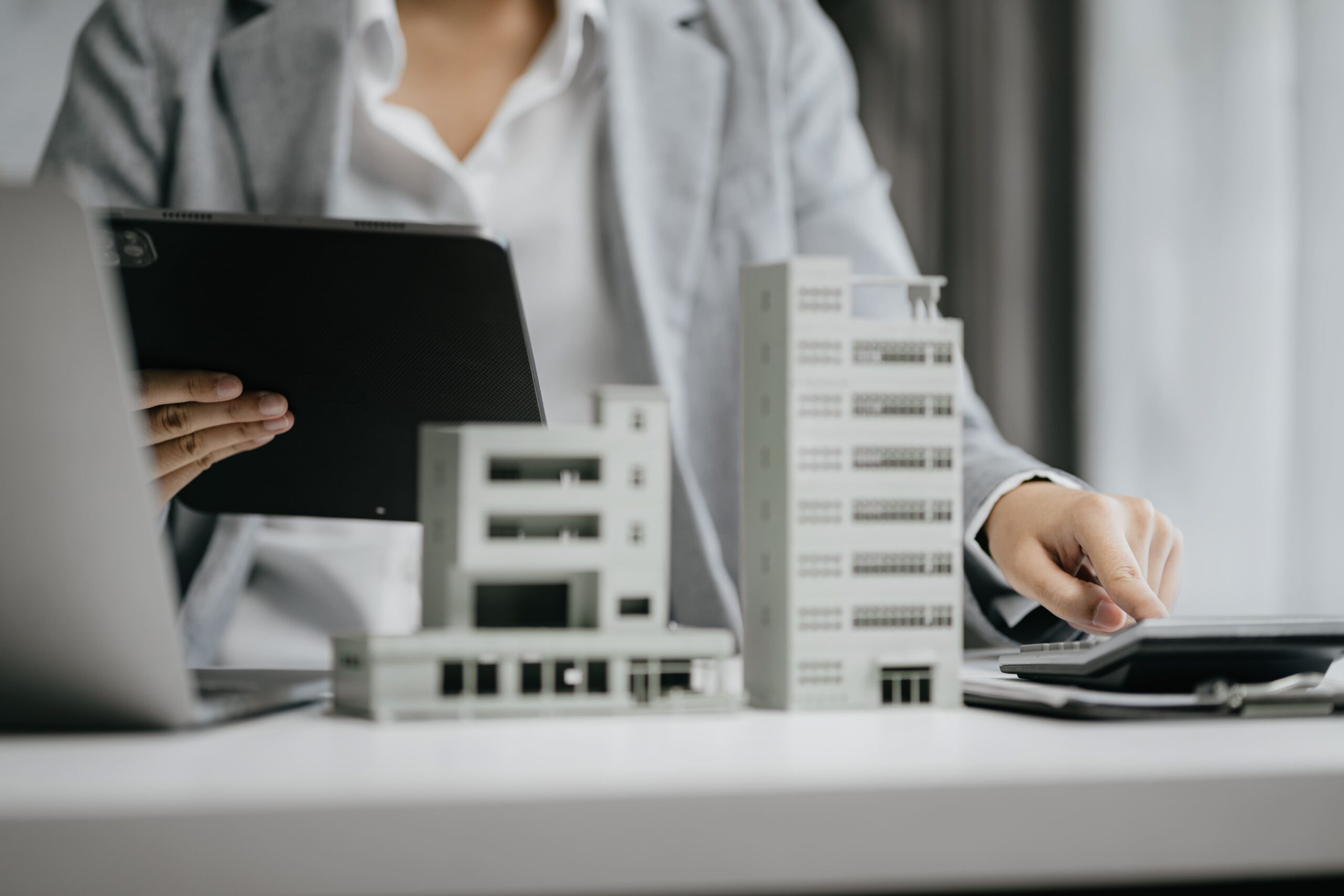 Person in Anzug arbeitet am Schreibtisch mit Gebäudemodellen.