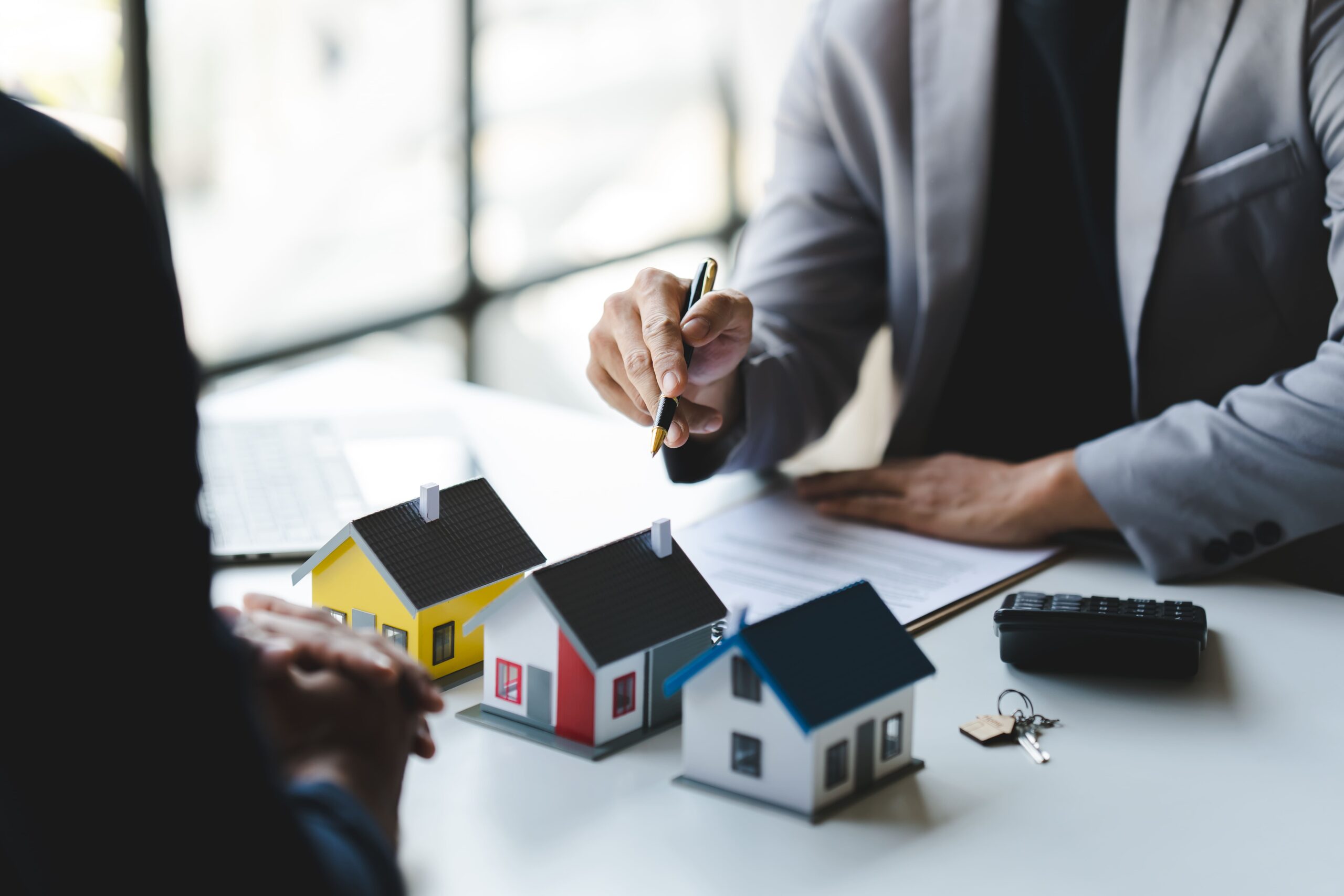 Zwei Personen besprechen Immobilien mit Papier und Modellhäusern.