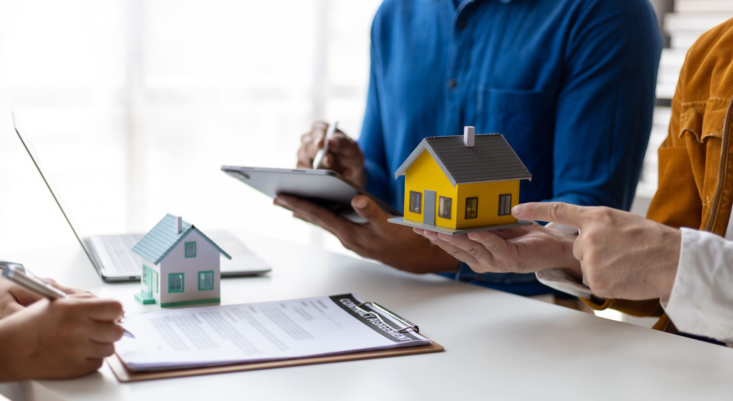 Drei Personen sprechen über Immobilien, mit Hausmodellen und Laptop.