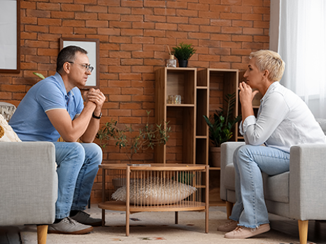 Zwei Personen sprechen ernsthaft auf Sofas im Wohnzimmer: Scheidungsimmobilie
