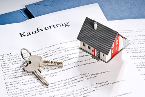Schlüssel und Miniaturhaus auf Vertrag mit Aufschrift "Kaufvertrag", Symbol für Immobilie verkaufen