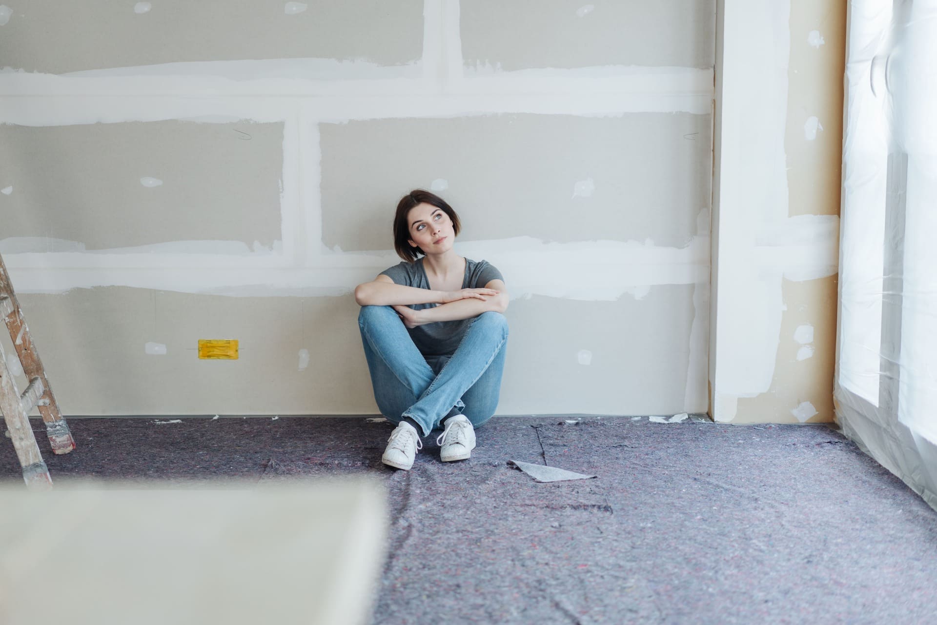 Frau sitzt auf dem Boden an einer unfertigen Wand und überlegt, ob sich due Aufwertung vor Verkauf lohnt