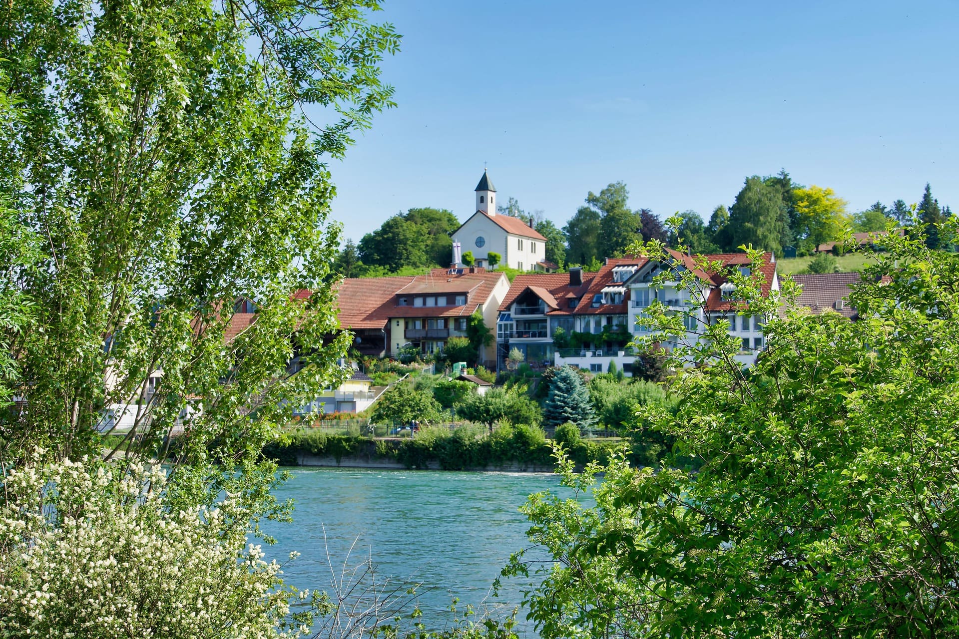 Dorf Häusern und Bäumen an Fluss unter blauem Himmel: Tipps für Investition in deutsche Immobilien
