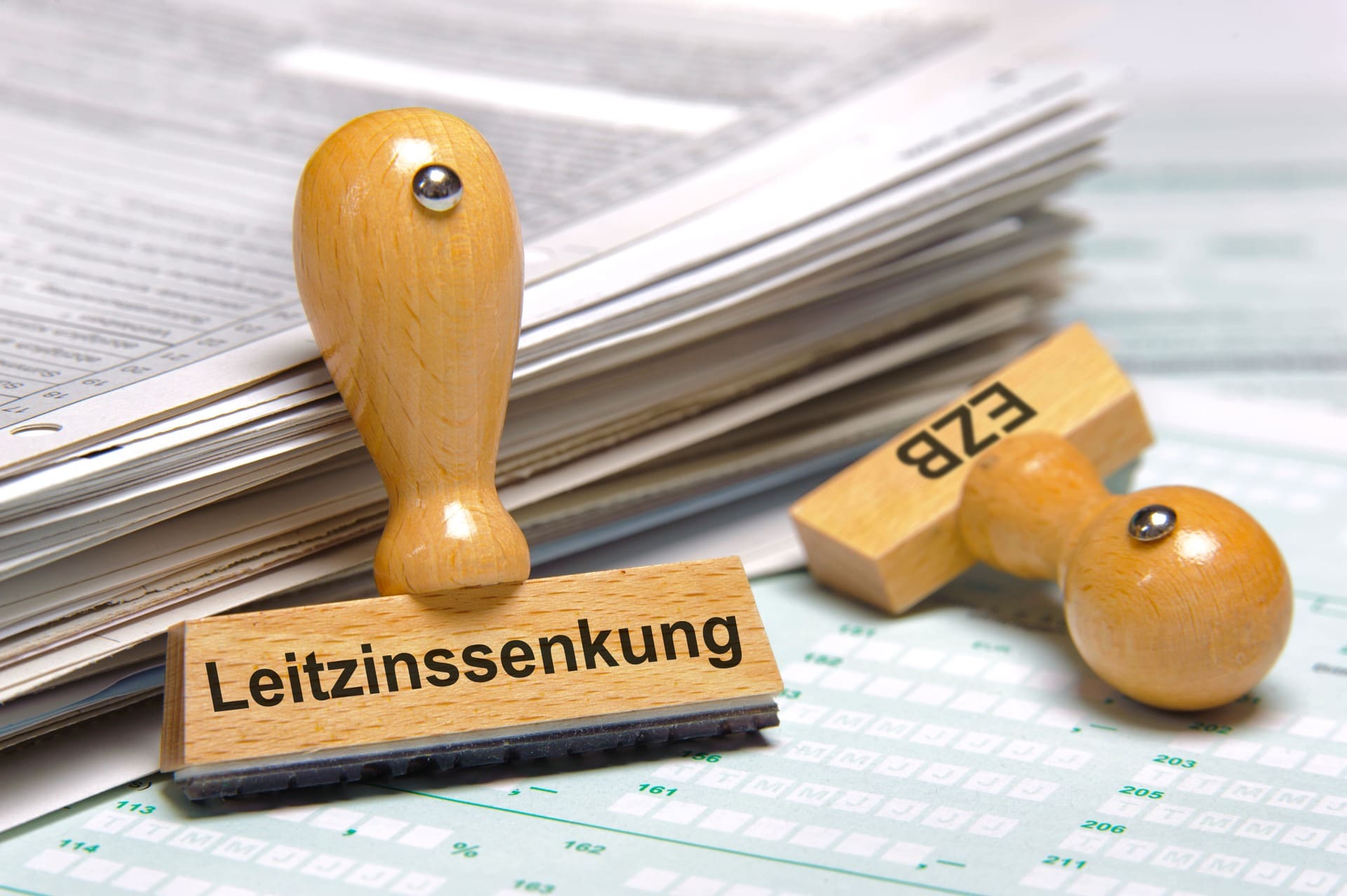 Holzstempel "Leitzinssenkung" und "EZB" auf Finanzdokumenten: Zinssenkung und Immobilienmarkt