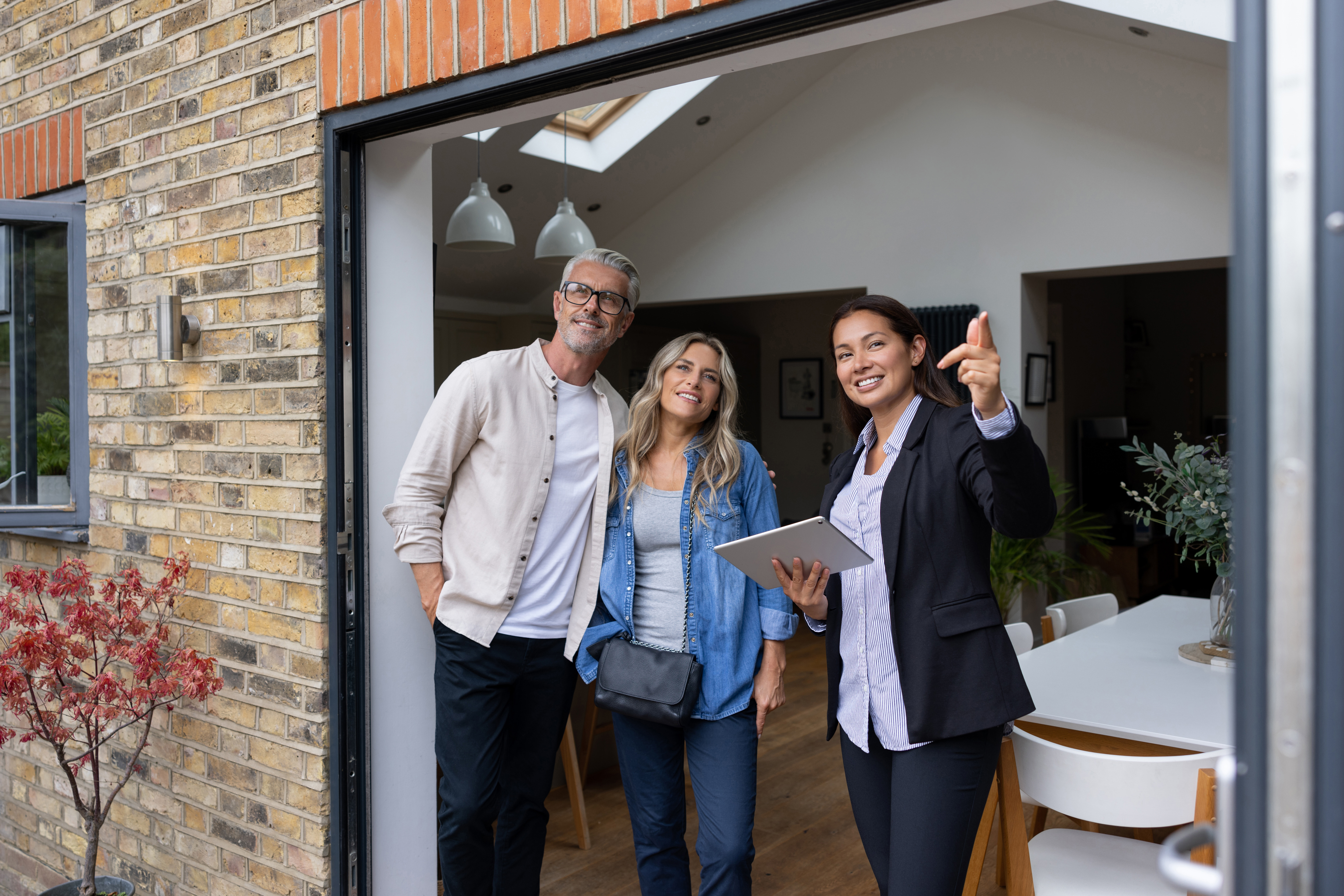 Immobilienmaklerin zeigt einem lächelnden Paar eine moderne Wohnimmobilie und erläutert Details während der Besichtigung.
