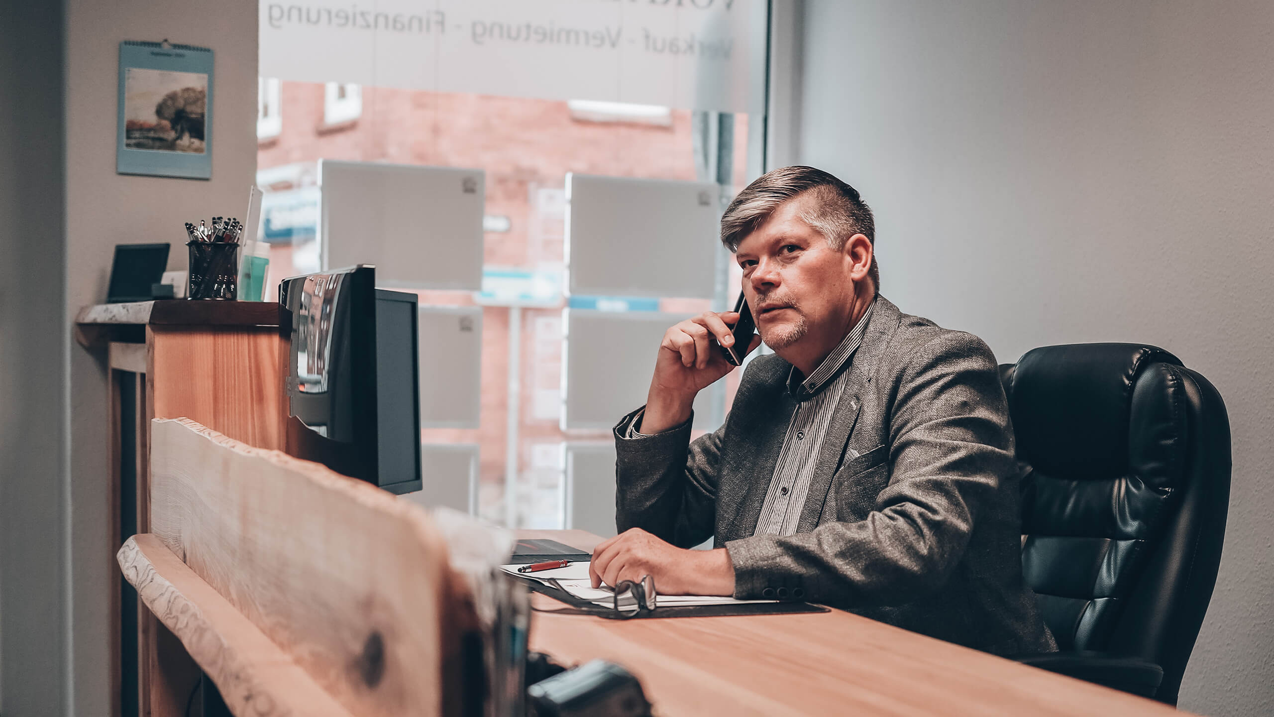 Herr Vorfahr im Anzug am Schreibtisch telefoniert nachdenklich.