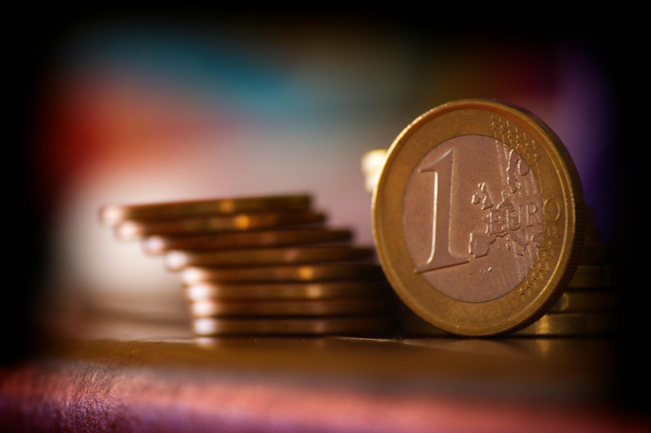 Gestapelte Euro-Münzen, ein Eurostück im Fokus, unscharfer Hintergrund.