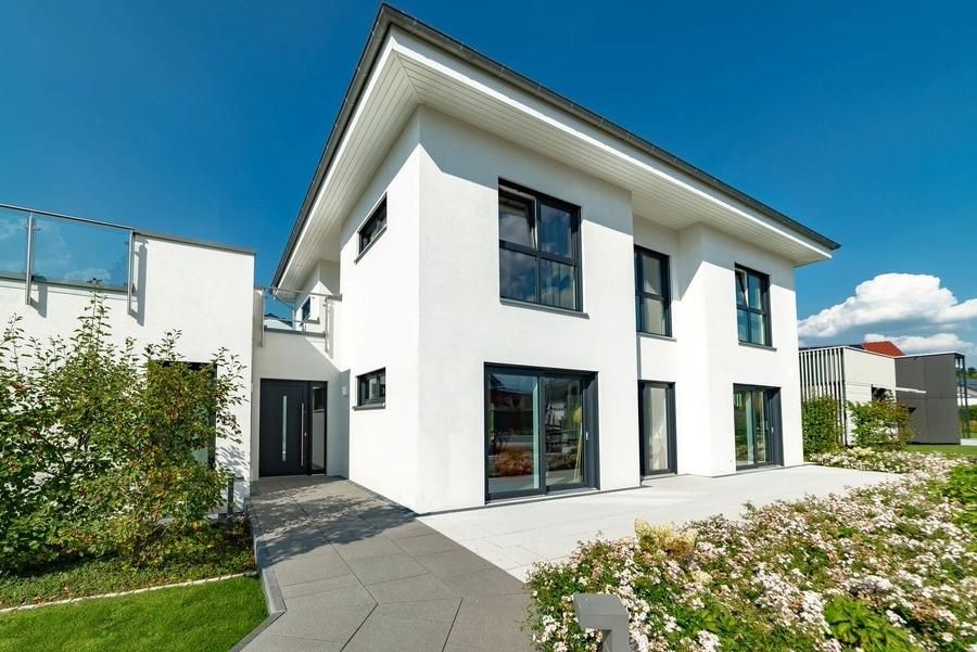 Zweistöckiges weißes Haus mit großen Fenstern und Garten.