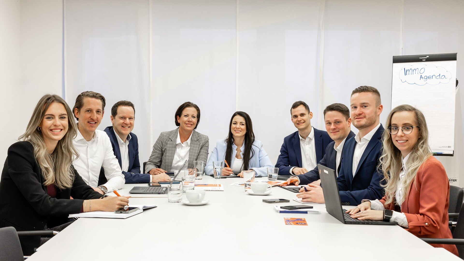 Team sitzt am Tisch und alle lächeln in die Kamera