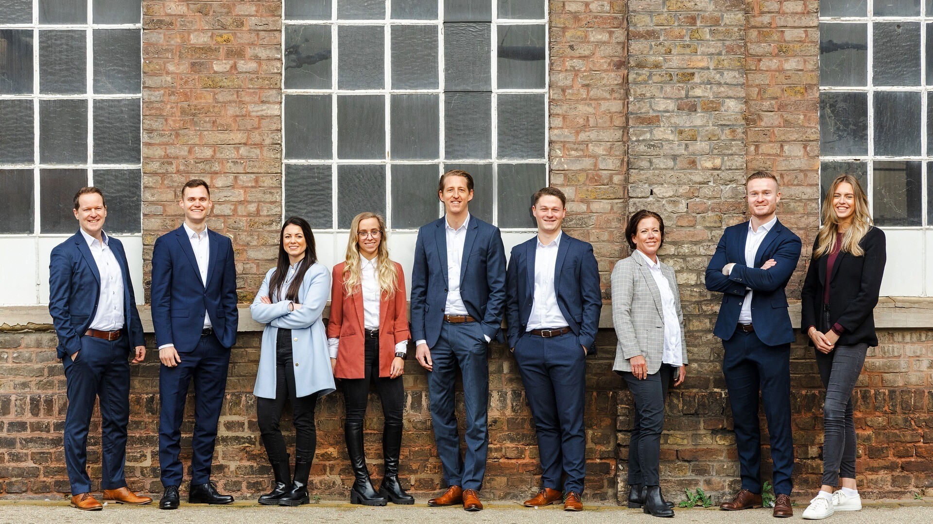 Team posiert nebeneinander vor einer Industriehalle