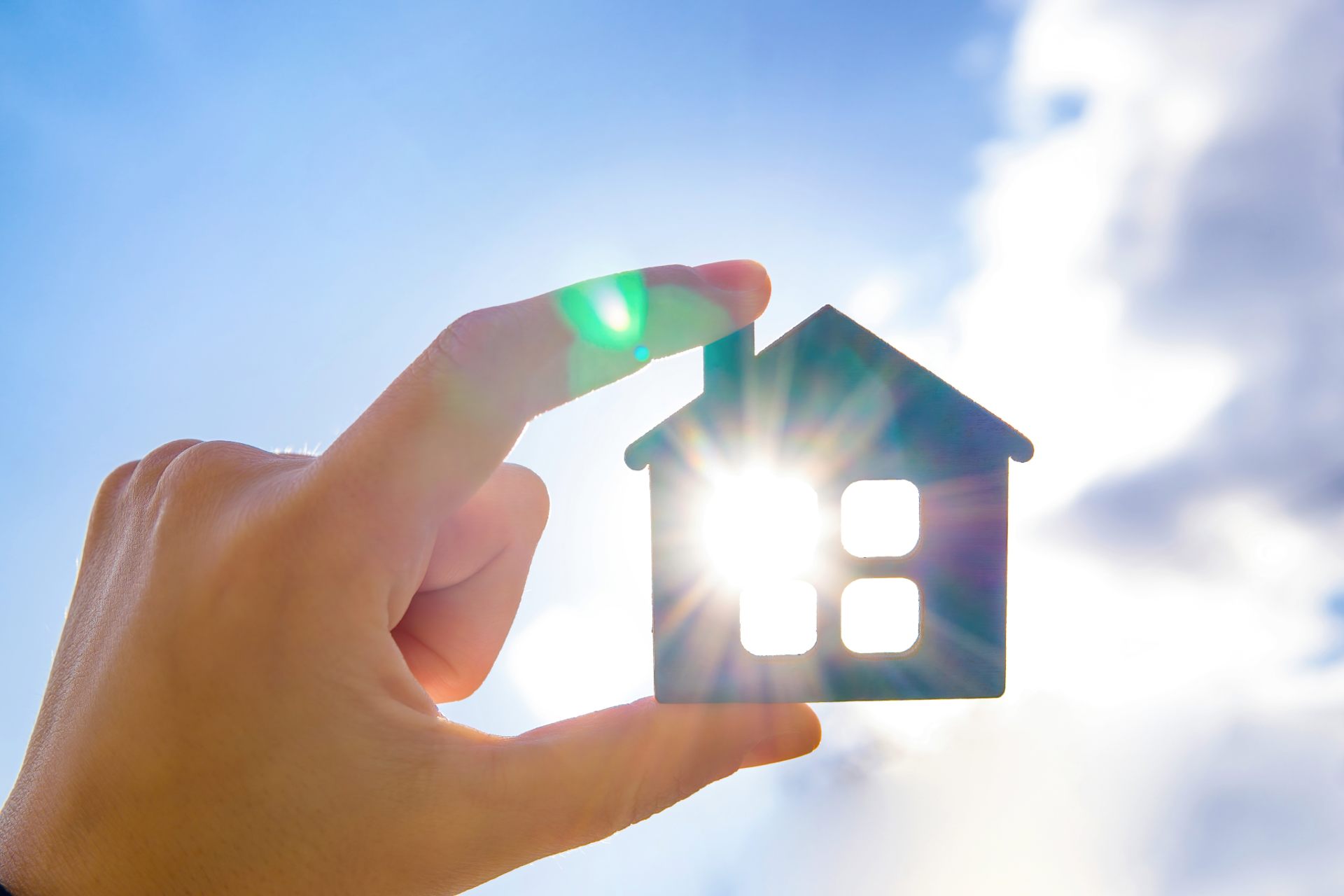 Person hält Miniaturhaus vor die Sonne